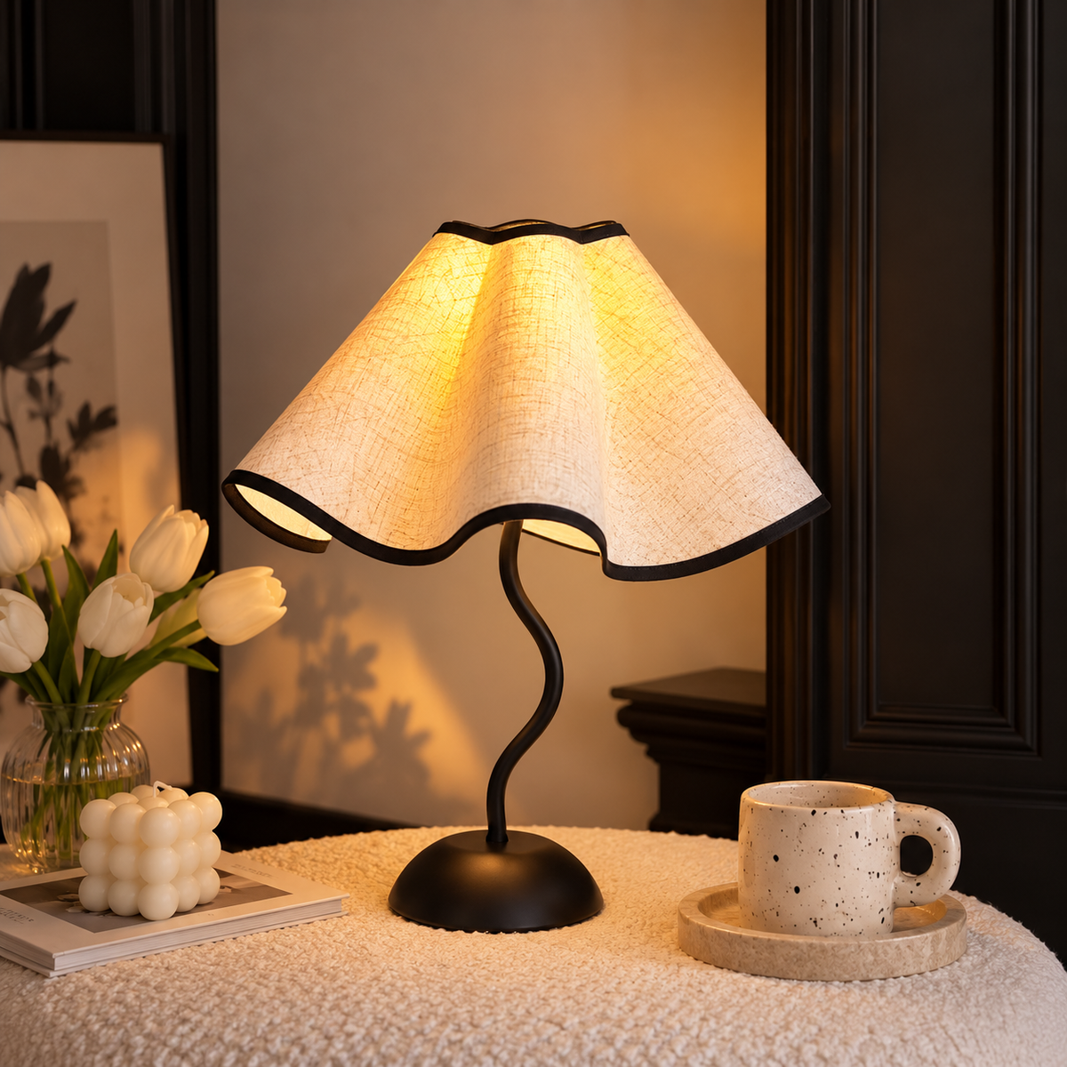 Petal table lamp casting a warm glow beside white tulips, a bubble candle and a speckled mug.