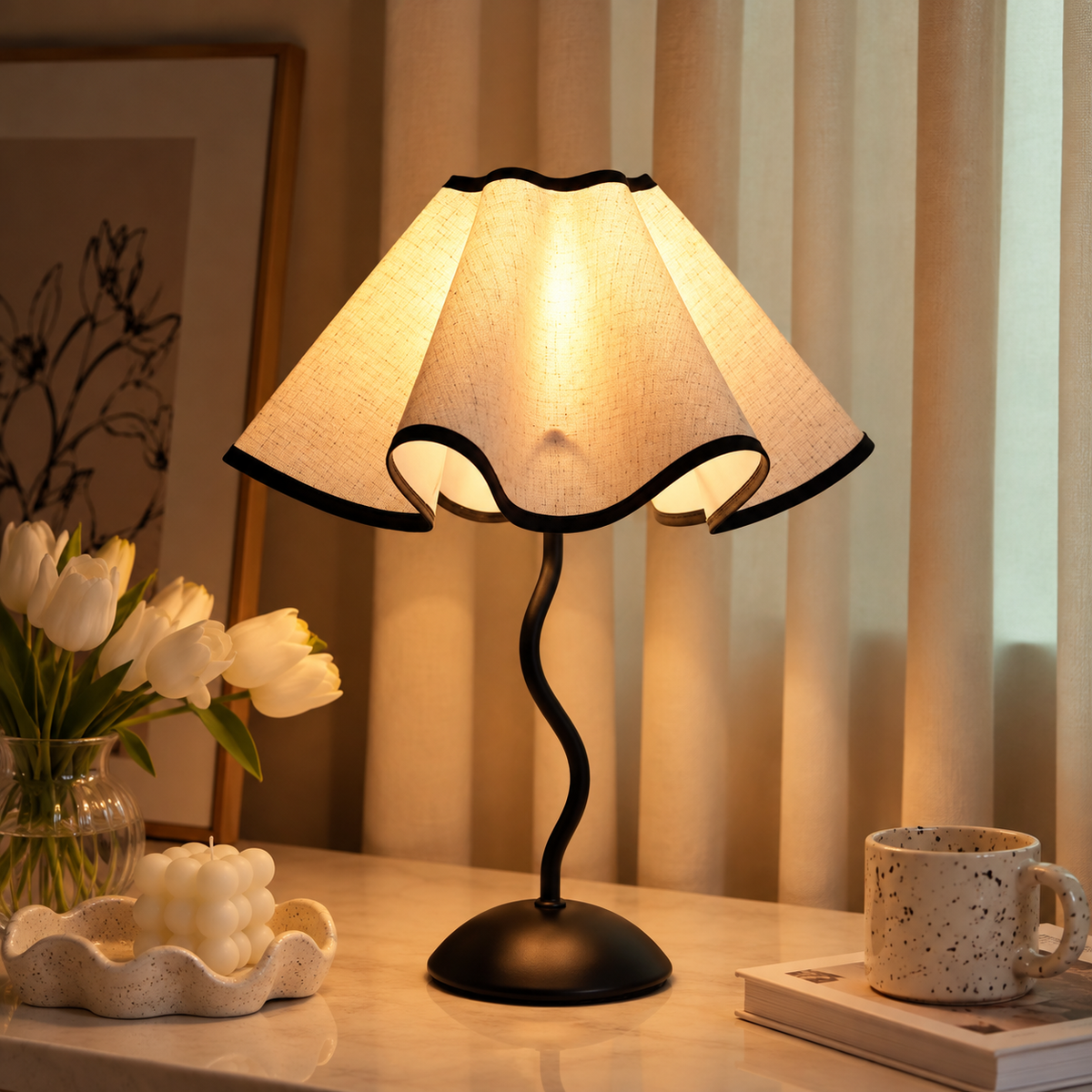 Illuminated cream petal shade with black trim and a curved black stem on a marble table beside tulips and a mug.