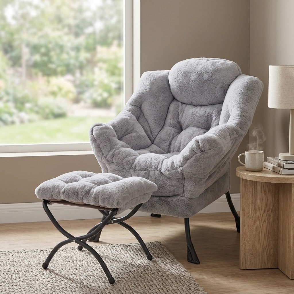 Light gray fuzzy plush lounge chair and matching padded ottoman with black legs, wood side table with a steaming mug, and a lamp by a window by HavvakHome.