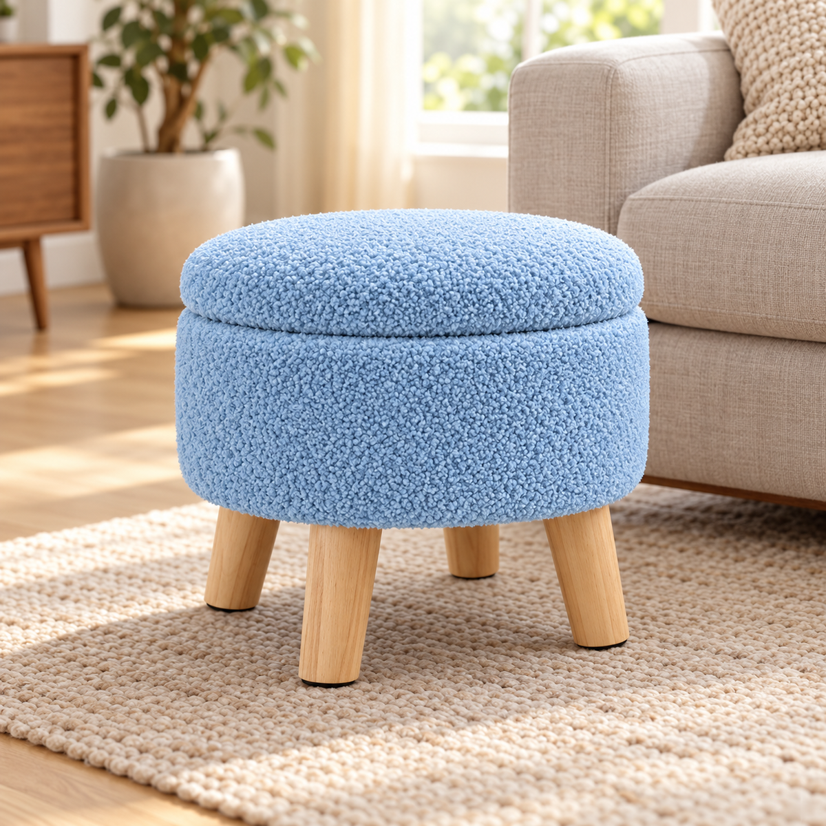 Blue nubby fleece round storage ottoman with four light wood legs and closed lid beside an oatmeal sofa.