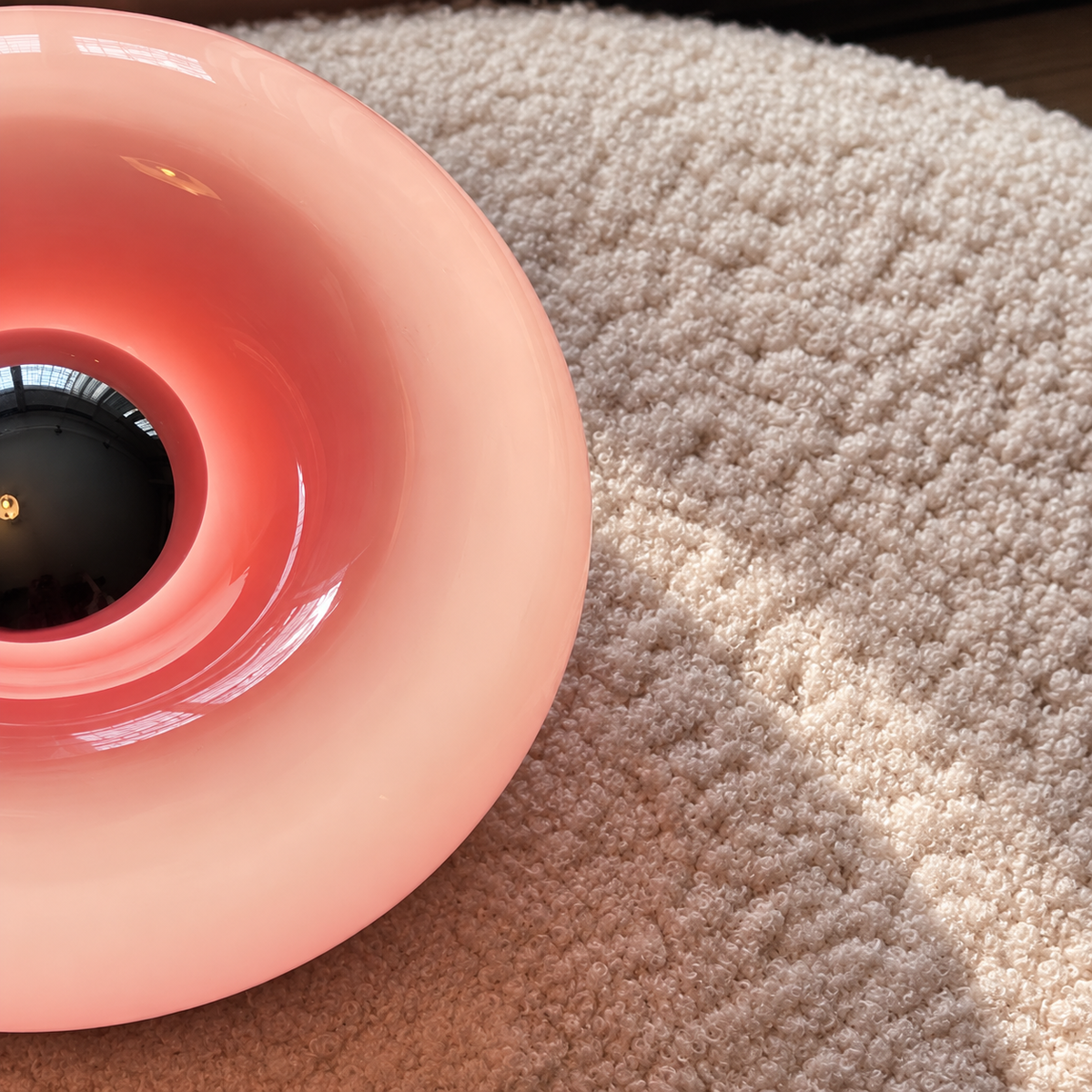 Close-up of the curved glossy pink shade and reflective center of a donut lamp on a cream rug.