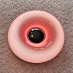 Top view of a glossy pink ring-shaped lamp with a reflective center on a cream textured rug.