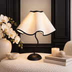 Cream scalloped lampshade and curved black base displayed with orchids, a candle and a decorative stone sphere.