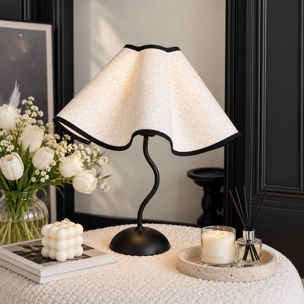 Cream petal lamp with black edging beside flowers, a candle and a reed diffuser in a bright room.
