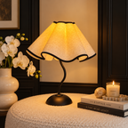 Warm glowing petal lamp on a textured table beside white orchids and books against dark wall panels.