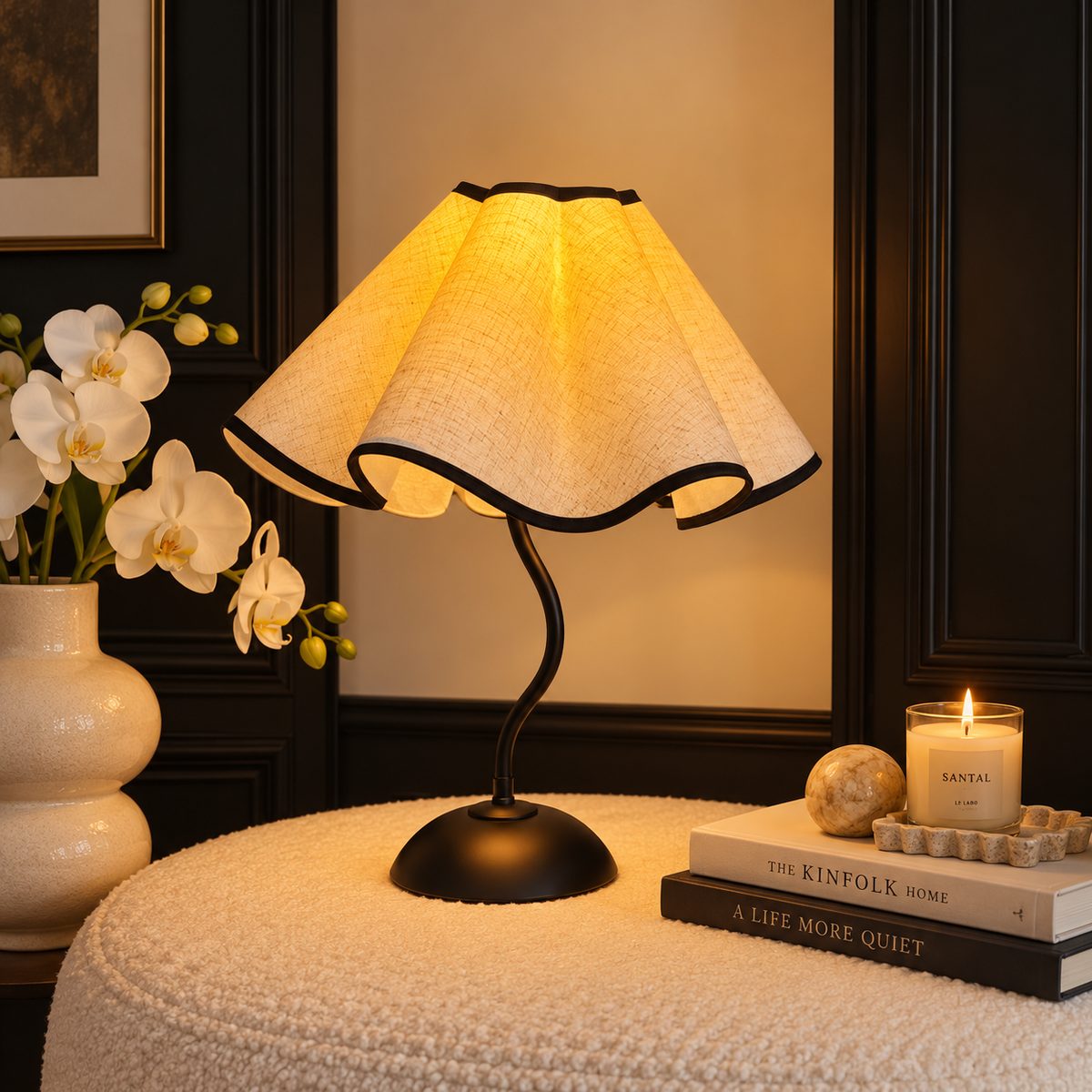 Warm glowing petal lamp on a textured table beside white orchids and books against dark wall panels.