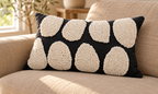 Black lumbar pillow cover with two rows of rounded cream tufted shapes on a tan sofa in sunlight.