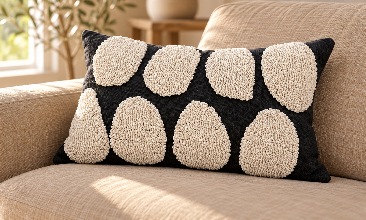 Black lumbar pillow cover with two rows of rounded cream tufted shapes on a tan sofa in sunlight.