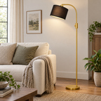Gold arc floor lamp with a tilted black shade beside a cream sofa.