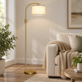 Gold arc floor lamp with a linen shade standing beside a cream sofa.