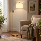 Gold arc floor lamp with a linen shade positioned next to a taupe armchair.
