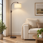Matte brown arc floor lamp featuring a beige linen shade beside a cream sofa.