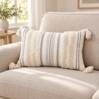 Beige and cream white 20x12 lumbar tufted pillow cover with tassels on an oatmeal sofa.