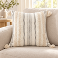 Beige and cream white square boho tufted pillow cover with tassels displayed on an oatmeal sofa.