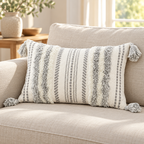 Grey and cream white 20x12 lumbar tufted pillow cover with corner tassels on an oatmeal sofa.