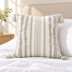 Grey and cream white square tufted pillow cover with woven rope details on a white bed.