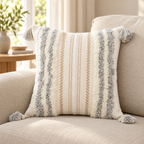 Light grey and cream white square tufted pillow cover with tassels on an oatmeal sofa.