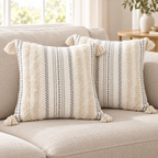 Two beige and cream white square tufted pillow covers with corner tassels on an oatmeal sofa.