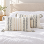 Pair of light grey and cream white 20x12 lumbar tufted pillow covers styled on a white bed.