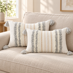 Two light grey and cream white 20x12 lumbar tufted pillow covers with tassels on an oatmeal sofa.