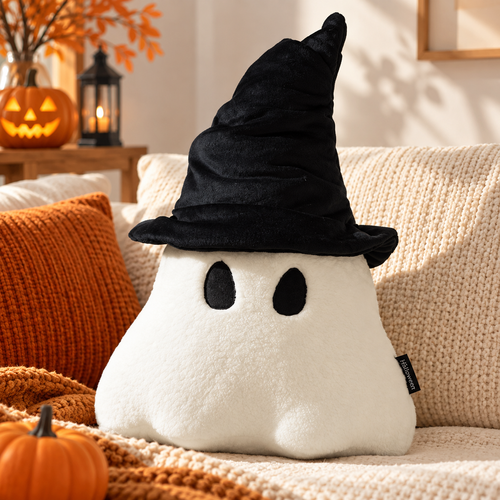 Off-white ghost pillow with a black witch hat on a cream sofa with an orange cushion, blanket, jack-o-lantern, and lantern in the background by HavvakHome.