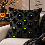 Single black raised ghost-pattern pillow with green eyes on a cream sofa styled with a dark knitted throw and jack-o-lantern background.