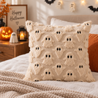 Single cream raised ghost-pattern pillow on a bed with an orange cushion, knitted blanket, jack-o-lantern, and lantern on the bedside table.