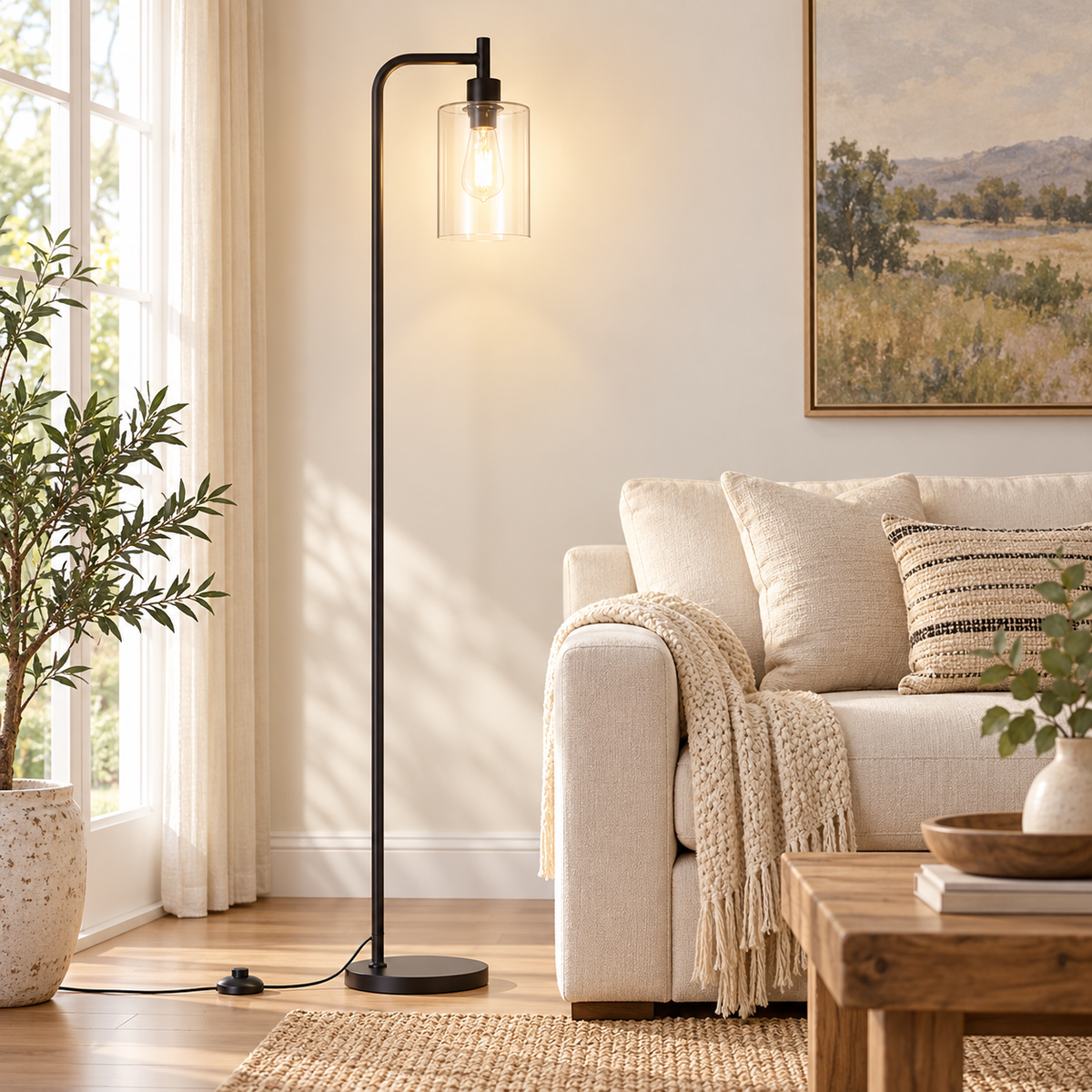 Black floor lamp with a clear cylindrical glass shade beside an ivory sofa in a sunlit living room.
