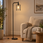 Smoke-grey glass black floor lamp next to an oatmeal armchair and wooden side table at dusk.