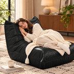 Woman resting curled on a black armless floor lounge chair beneath a cream knitted throw in a living room by HavvakHome.