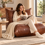 Woman reading a book on a brown armless floor lounge chair with a cream knitted throw beside a wood side table and window by HavvakHome.