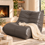 Gray button-tufted armless floor lounge chair with a cream knitted throw on a rug beside a fireplace and a window by HavvakHome.