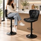 Woman holding a mug seated on a black quilted bar stool beside a second black bar stool with black pedestal bases and footrests at a kitchen island by HavvakHome.