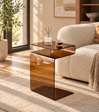 Amber S-shaped glass side table beside a cream armchair holding a coffee glass and reed diffuser by HavvakHome.