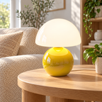 Yellow ceramic mushroom lamp with a glossy rounded base and a white glass dome shade on wooden furniture in a naturally lit living room.