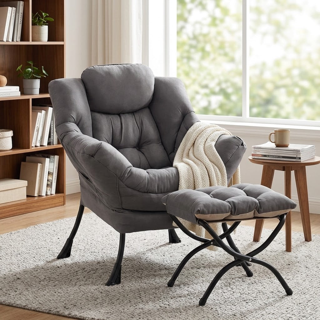 Gray plush lounge chair and matching foldable ottoman with black metal legs and cream throw over right arm beside a bookshelf and side table by a window by HavvakHome.
