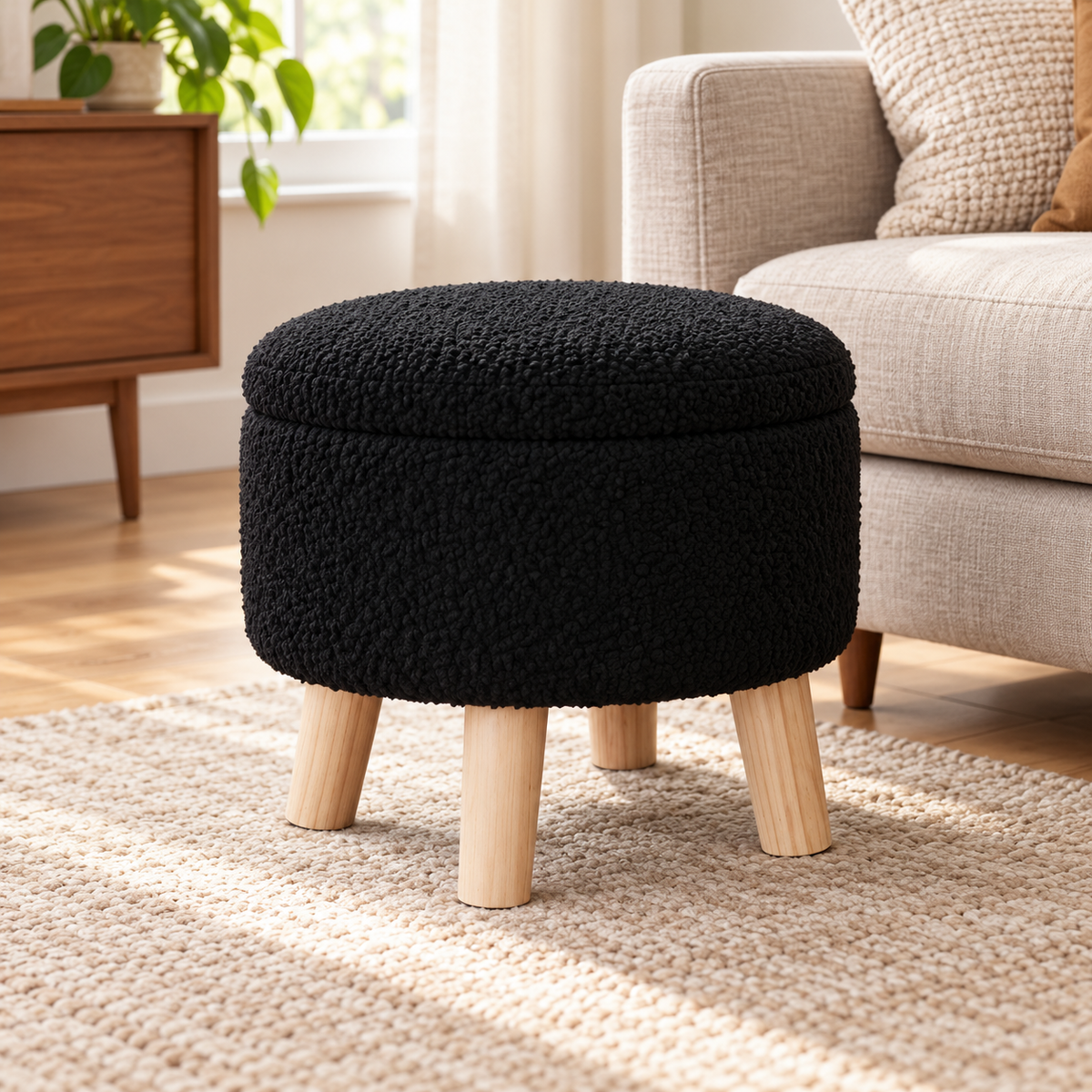 Black nubby fleece round storage ottoman with four light wood legs and closed lid beside an oatmeal sofa.