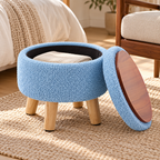 Blue round storage ottoman with lid set aside showing wood-grain underside and black storage interior with folded cloth.