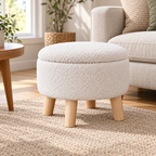Cream nubby fleece round storage ottoman with four light wood legs and closed lid on a light oak floor.