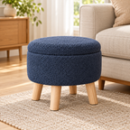 Dark grey-blue nubby fleece round storage ottoman with four light wood legs and closed lid on a light oak floor.