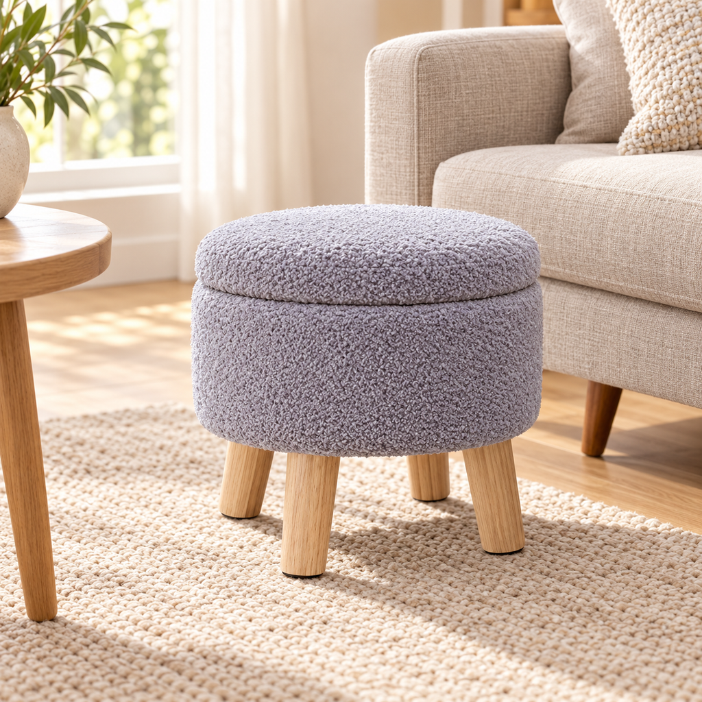 Grey nubby fleece round storage ottoman with four light wood legs and closed lid beside an oatmeal sofa.
