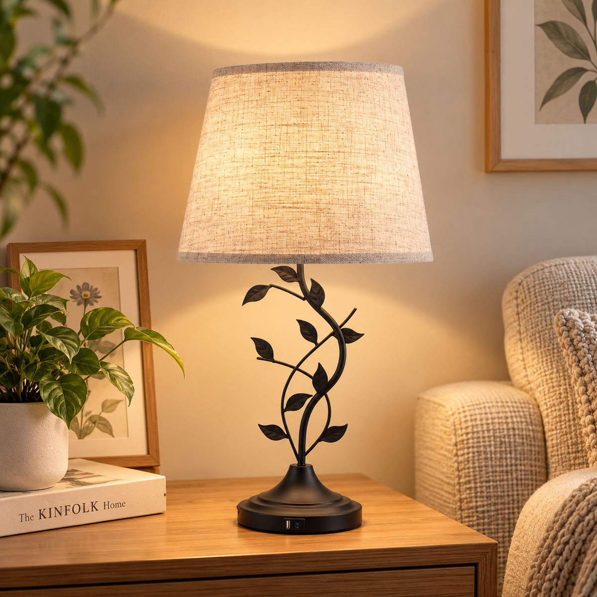Glowing leaf-vine table lamp with beige shade on a wood side table beside an upholstered armchair, plant, and framed botanical artwork by HavvakHome.