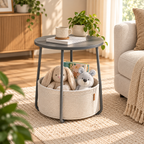 Gray round side table with a cream basket holding a plush bunny, bear, and book beside a light sofa, with a plant and mug on the tabletop by HavvakHome.