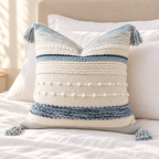 Coastal blue 18x18 inch throw pillow cover with horizontal textured stripes and corner tassels arranged on a white bed against a beige headboard.