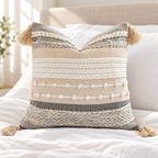 Gray 18x18 inch square pillow cover showing horizontal textured stripes and tassels on a white bed against a beige headboard.