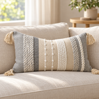 Gray 20x12 inch lumbar pillow cover featuring vertical textured stripes and four corner tassels on an oatmeal linen sofa.