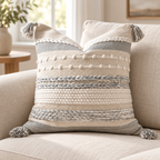 Gray and white 18x18 inch pillow cover featuring horizontal stripes, braids, and four corner tassels on an oatmeal linen sofa.