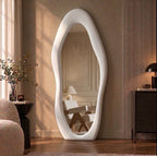 White irregular wavy flannel-framed full-length mirror leaning beside a wood-slat wall, reflecting an armchair.
