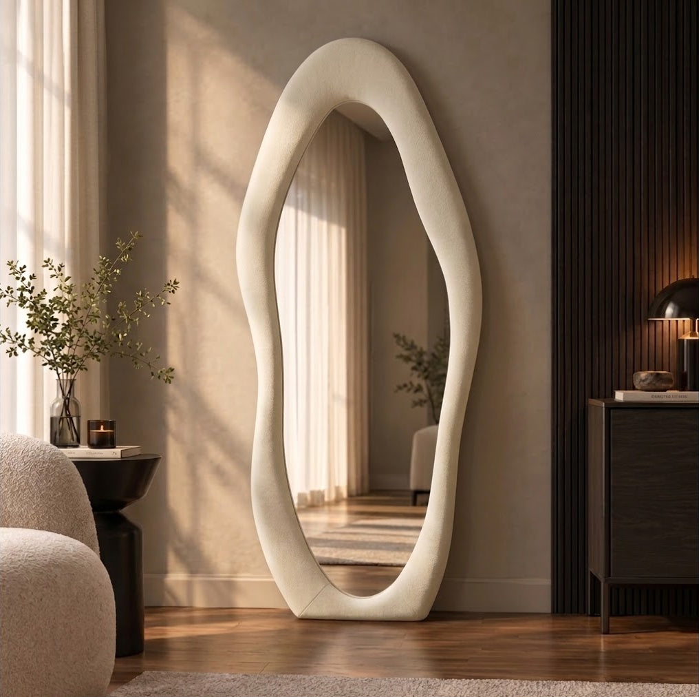 Cream wavy flannel-framed floor mirror leaning beside a wood-slat wall, reflecting window curtains.
