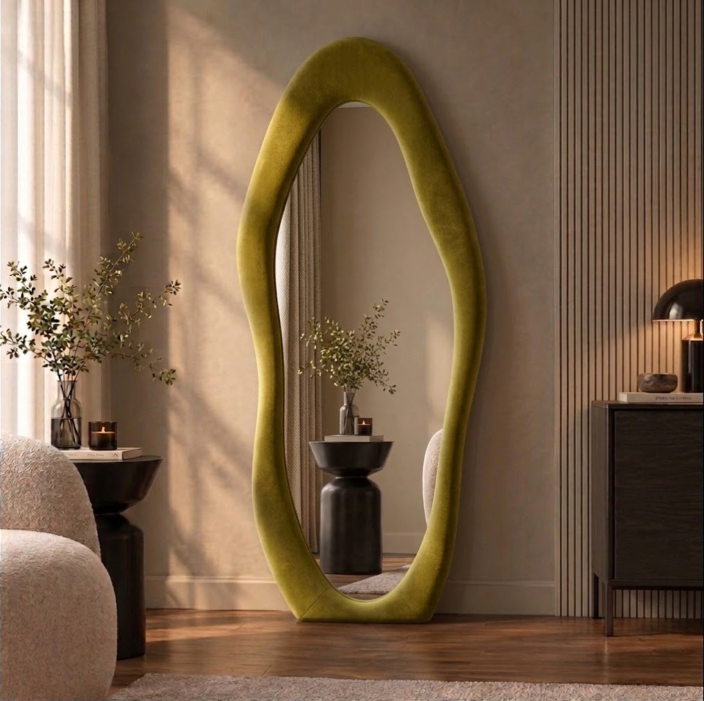 Olive green wavy flannel-framed floor mirror leaning beside a wood-slat wall, reflecting a vase on a side table.